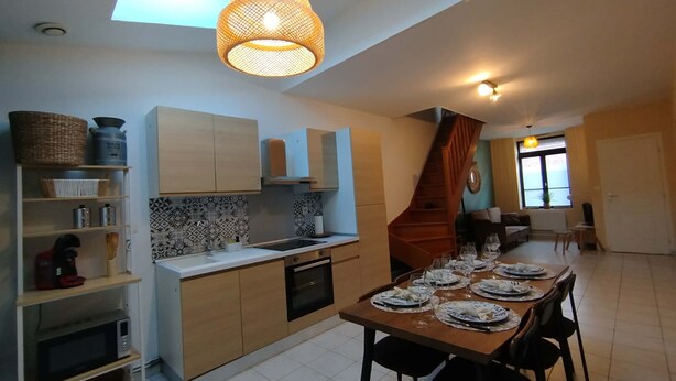 Une cuisine moderne avec des meubles en bois, un lave-vaisselle et un coin repas avec une table dressée pour six personnes.