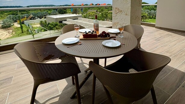 Een ronde tafel met stoelen op een balkon, met uitzicht op een schilderachtig landschap vol groen en een heldere lucht.