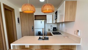 Een moderne keuken met een centraal eiland, twee hangende rieten hanglampen en drie barkrukken.