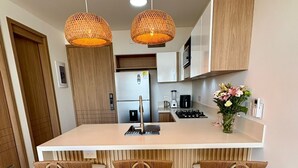 Een moderne keuken met een centraal eiland, drie barkrukken en hangende rieten pendelverlichting.