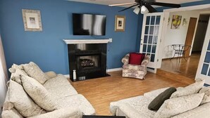 Una sala de estar con dos sofás estampados, una chimenea y un televisor en la pared.
