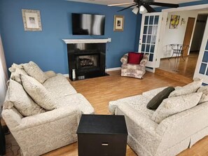 Una sala de estar con dos sofás estampados, una chimenea y un televisor en la pared.