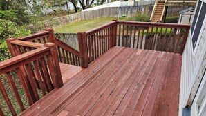 Una terraza de madera con barandilla, rodeada por un césped y una valla de madera.