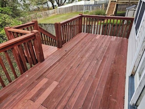 Una terraza de madera con barandilla, rodeada por un césped y una valla de madera.