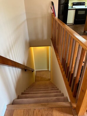 A wooden staircase with a handrail, leading to a landing with a kitchen area in the background. - Country Knoll 4/2 with 6 beds (Saint Charles)