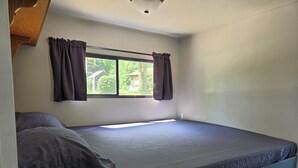 Un lit simple avec une tête de lit, une fenêtre avec des rideaux et un luminaire au plafond.