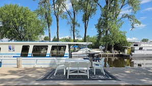 Une jetée avec un bateau, une table, des chaises et une zone herbeuse.