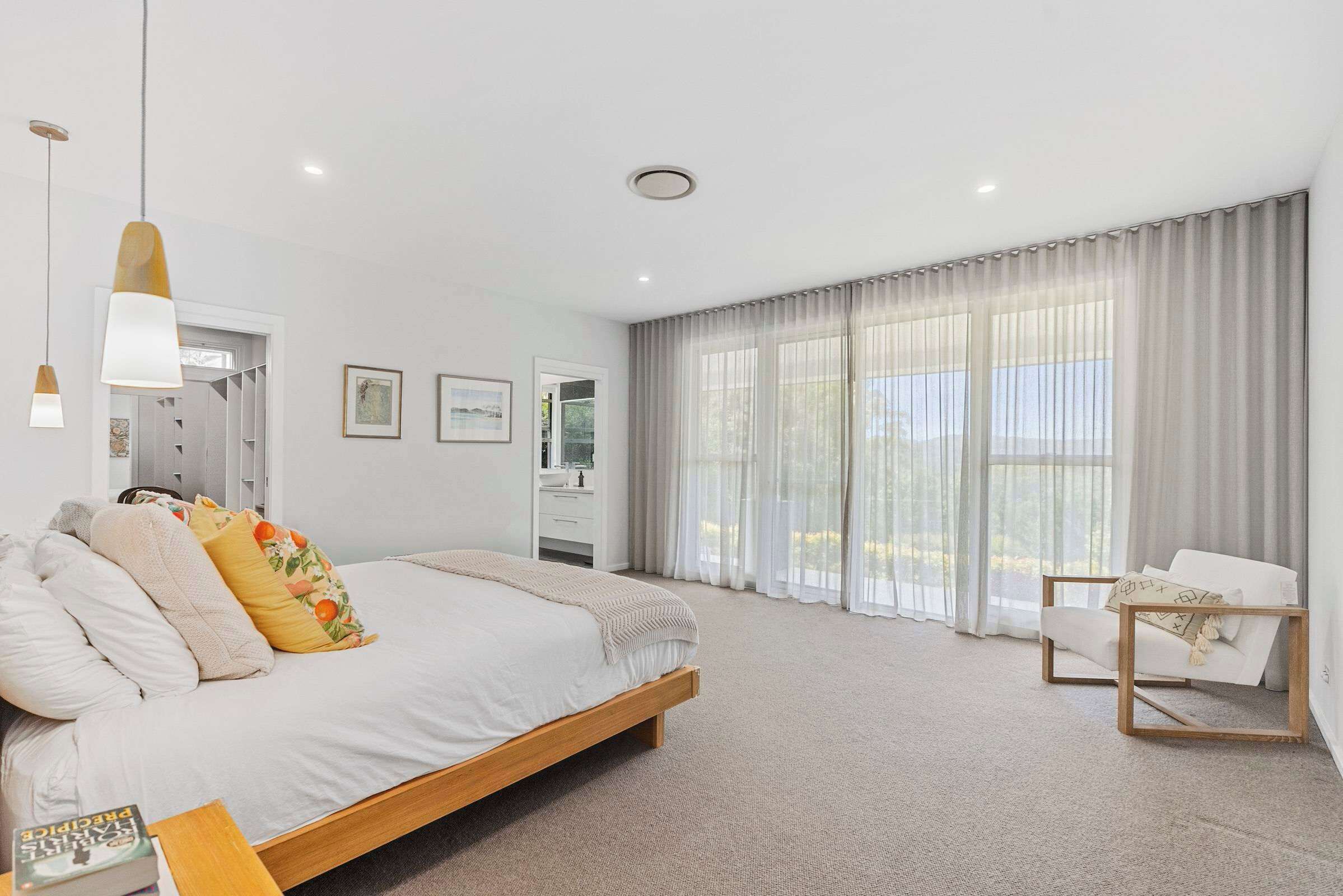A modern bedroom with a large bed, a bedside table, a chair, and a window with curtains.