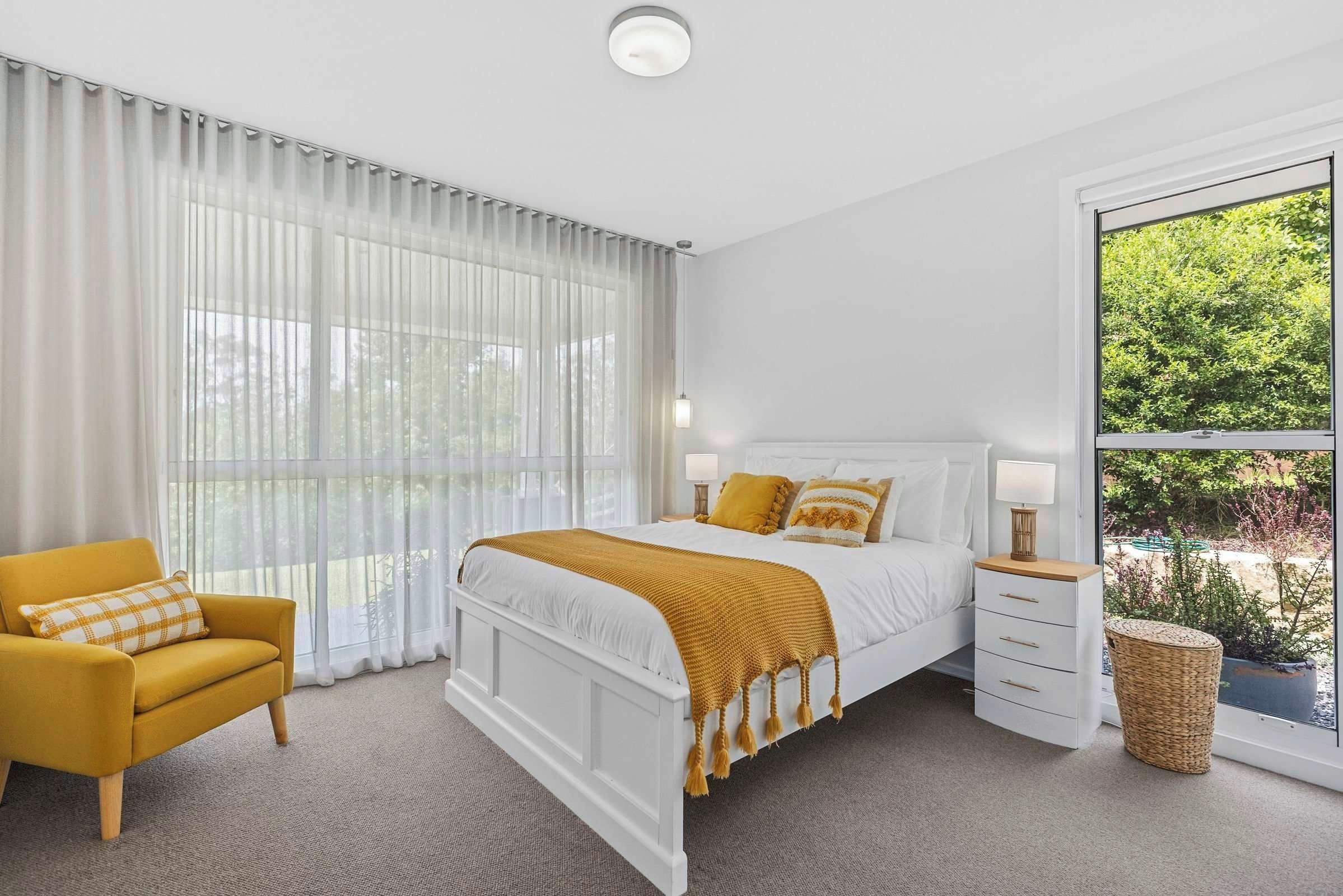 A bedroom with a bed, a chair, a nightstand, and a window with a view of greenery.