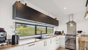 A modern kitchen with a large window, stainless steel appliances, and a view of a green landscape.