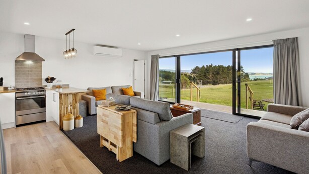 A modern living room with a grey sofa, wooden coffee table, and a large sliding glass door leading to a grassy outdoor area.