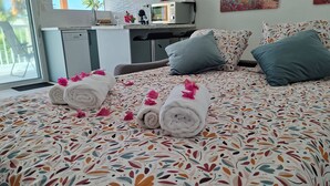 Habitación de hotel con una cama con cubrecama estampado floral, un escritorio con microondas y una ventana con vistas a palmeras.