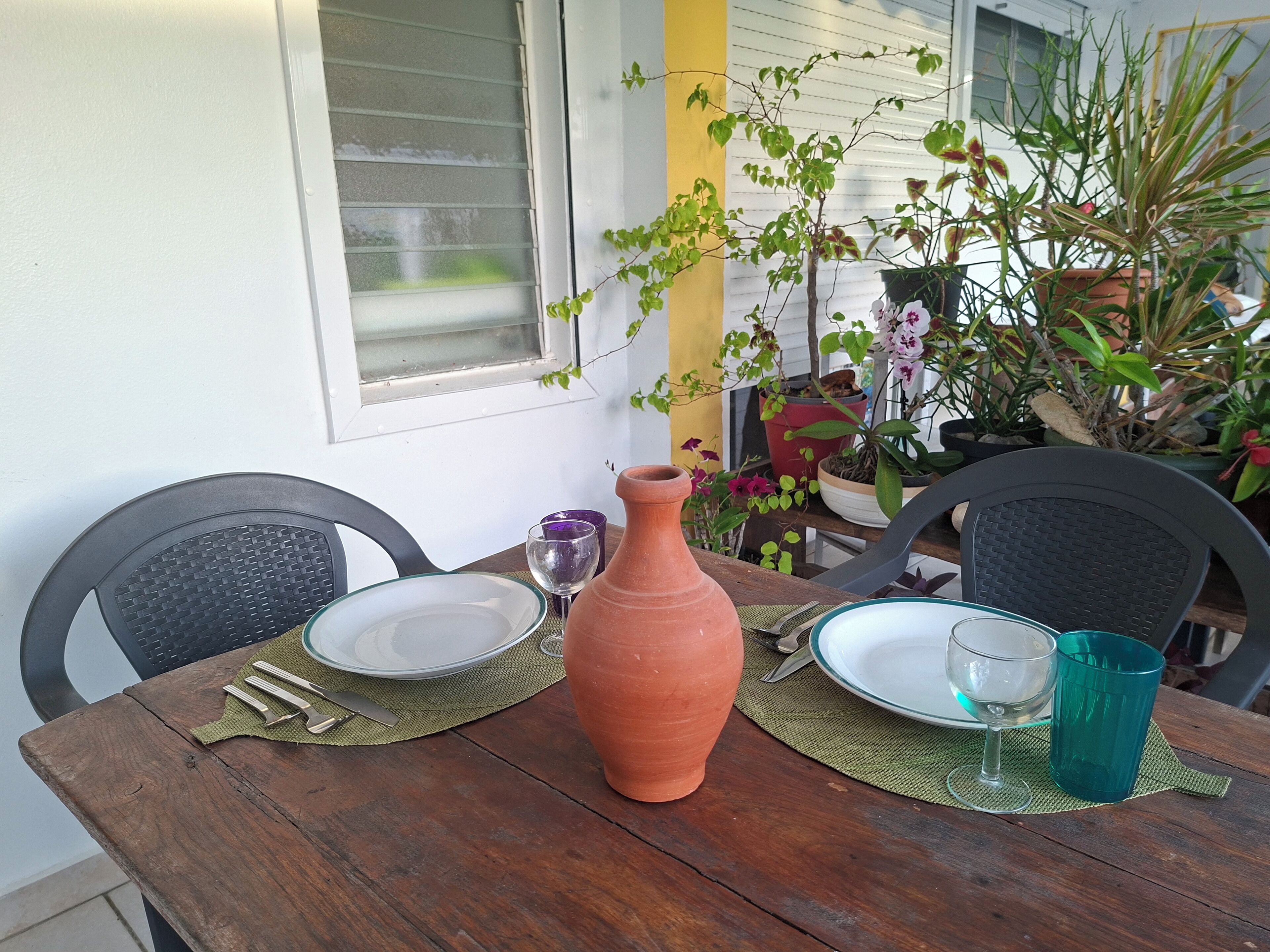 A wooden table with a terracotta vase, two plates, and two glasses.