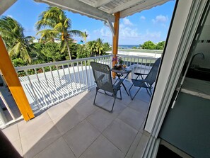 Un balcon avec vue sur l’océan, comprenant deux chaises et une petite table sur laquelle sont posés une boisson et des fruits.