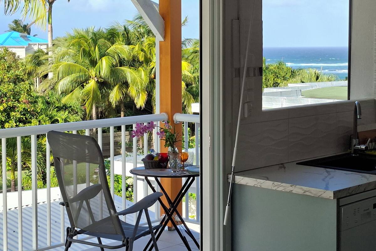 Un balcón con vistas al océano, una mesita con una silla y una zona de cocina.