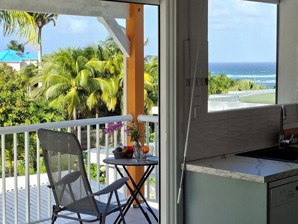 Un balcon avec vue sur l’océan, une petite table avec une chaise et un coin cuisine.