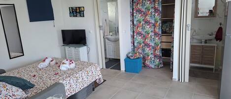 A bedroom with a bed, a TV, a bathroom with a sink and mirror, and a dining area with a table set for two.