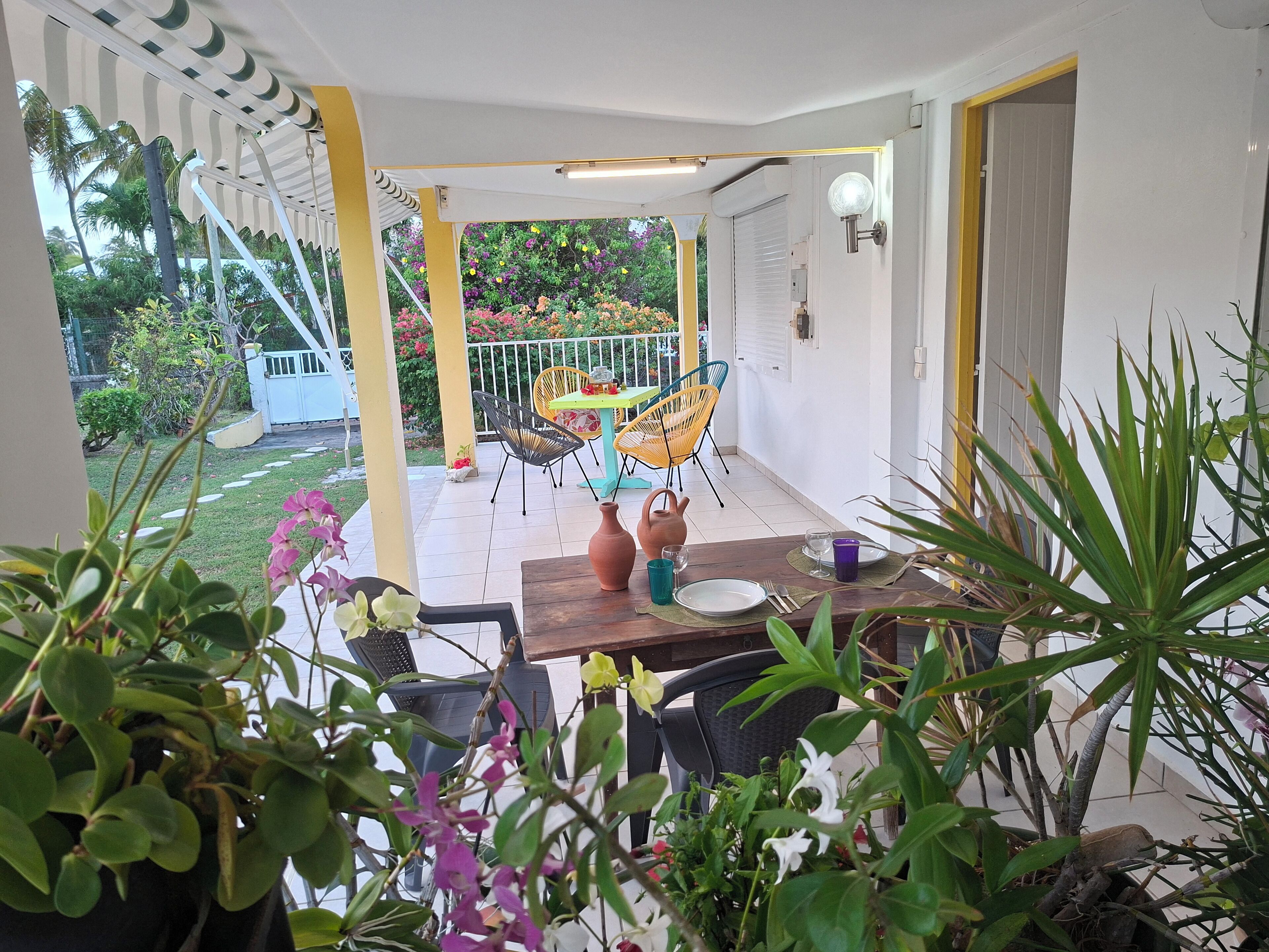 Un espace extérieur abrité, aménagé pour prendre les repas, avec une table pour deux, entouré de plantes en pot et de chaises.