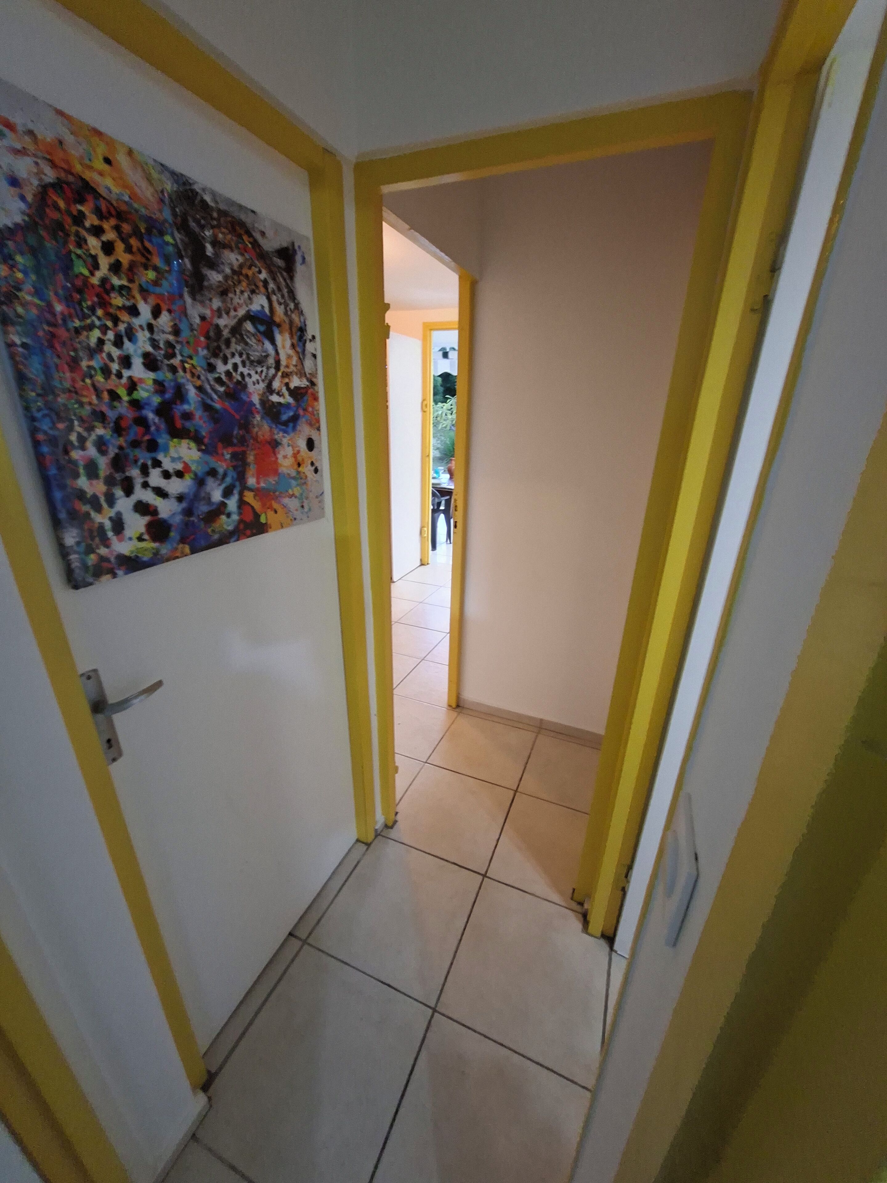 Un pasillo estrecho con detalles en amarillo, piso de baldosas y una puerta que da a otra habitación.