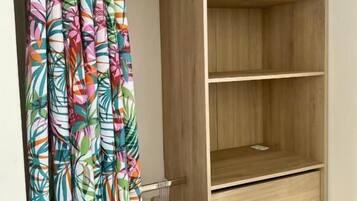 A wooden wardrobe with multiple shelves and drawers, a hanging rack with clothes, and a curtain with a tropical leaf pattern.