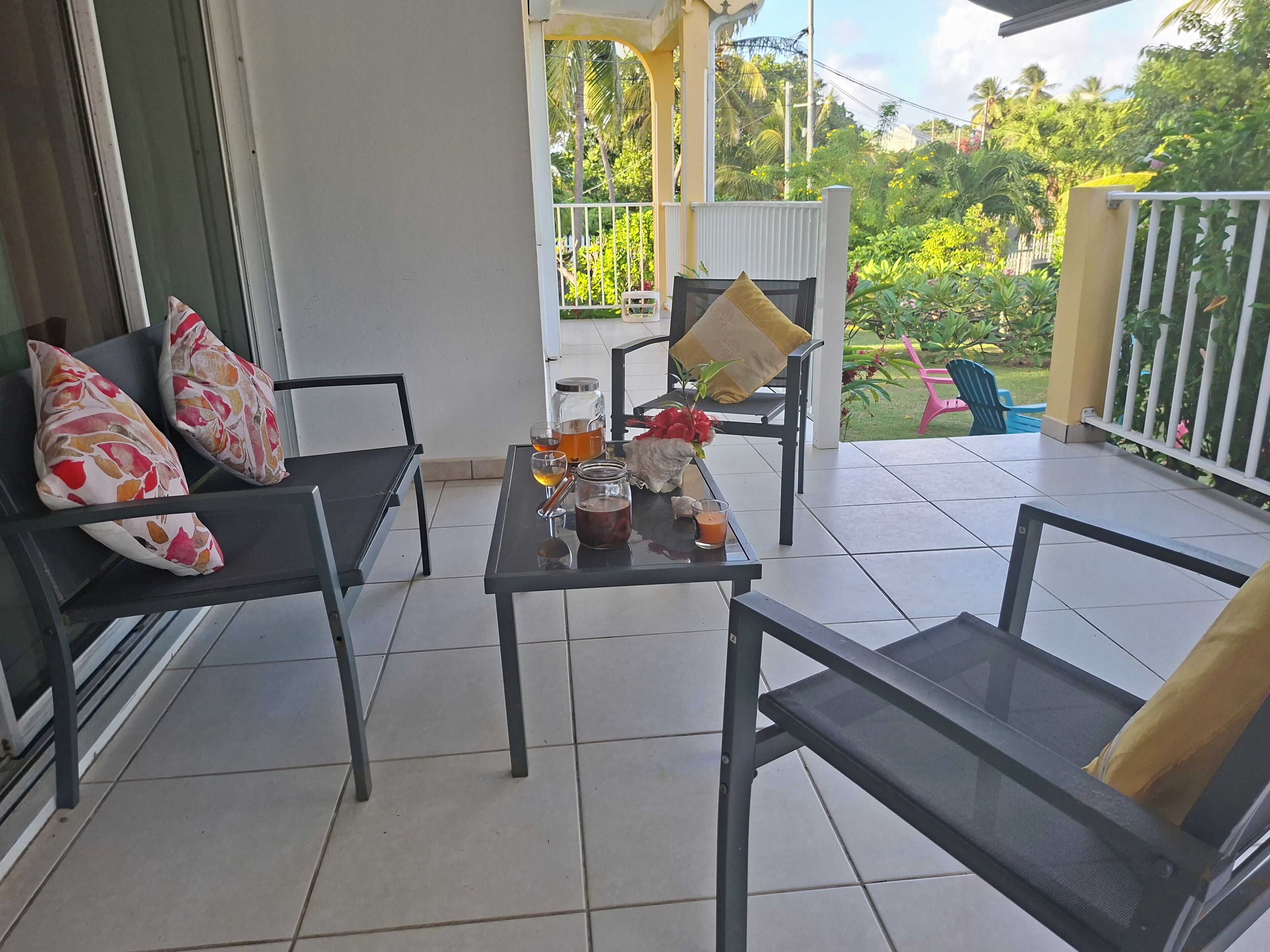 A balcony with two chairs, a table with drinks, and a view of greenery.