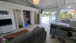 Una sala moderna con sofá, televisión, espacio de cocina con taburetes de bar y puerta corrediza de vidrio que da a un balcón.