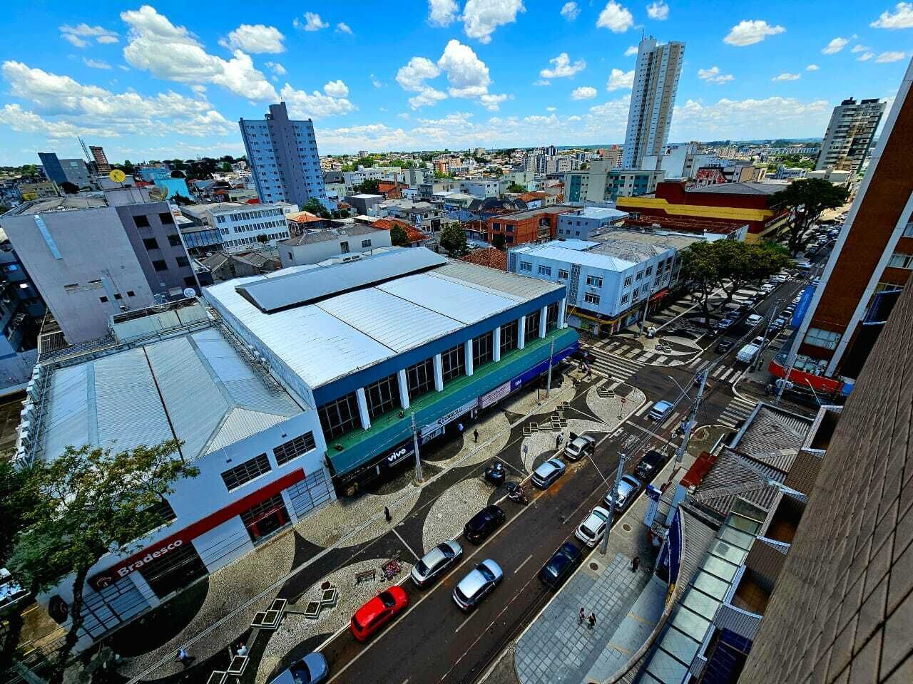 An aerial view of a cityscape with a prominent building featuring a blue and white facade, surrounded by other buildings and a busy street with cars.