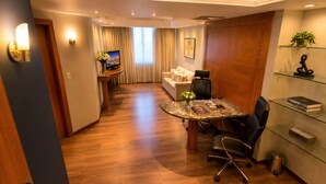 A hotel room with a dining area, a sofa, a TV, and a desk with a computer. - Santoni Hotel Guarapuava (Guarapuava)