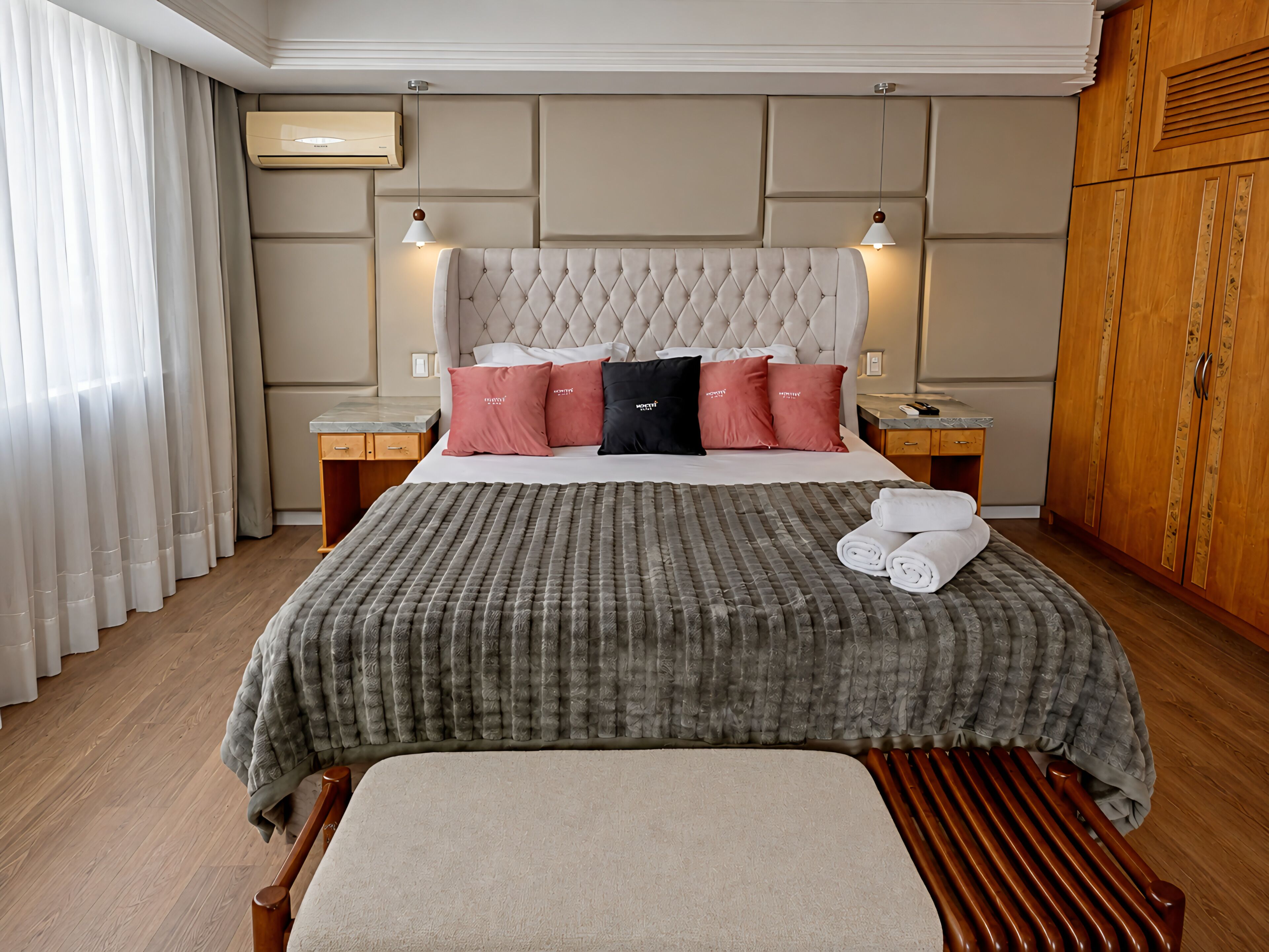 Habitación de hotel con una cama grande, dos mesitas de noche, un armario y una ventana con cortinas.