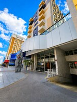Un hotel moderno con una entrada destacada, amplias ventanas y cielo despejado.