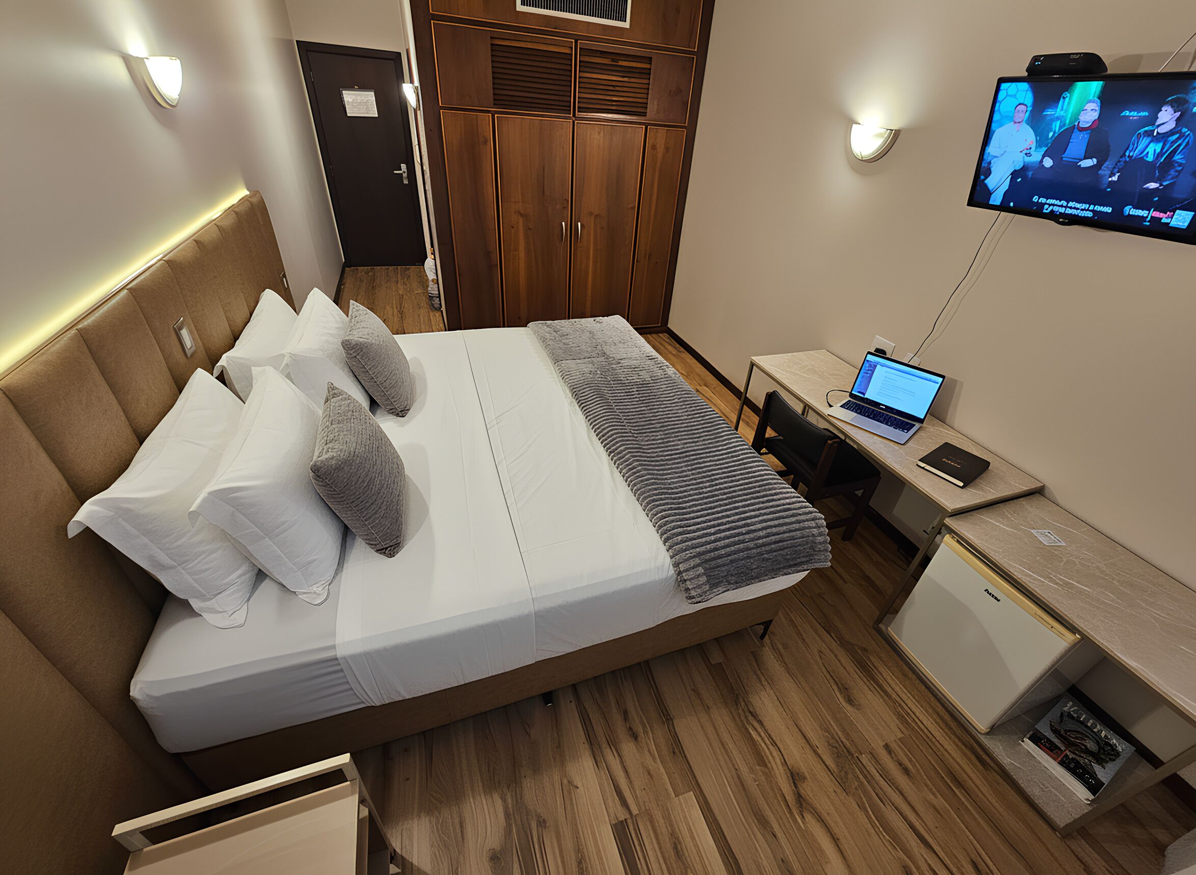 A hotel room with a bed, bedside table, desk, and a TV mounted on the wall.