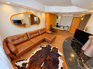 Un salon moderne avec un canapé en cuir marron, un grand miroir, un pouf en cuir noir et un tapis en peau de vache.