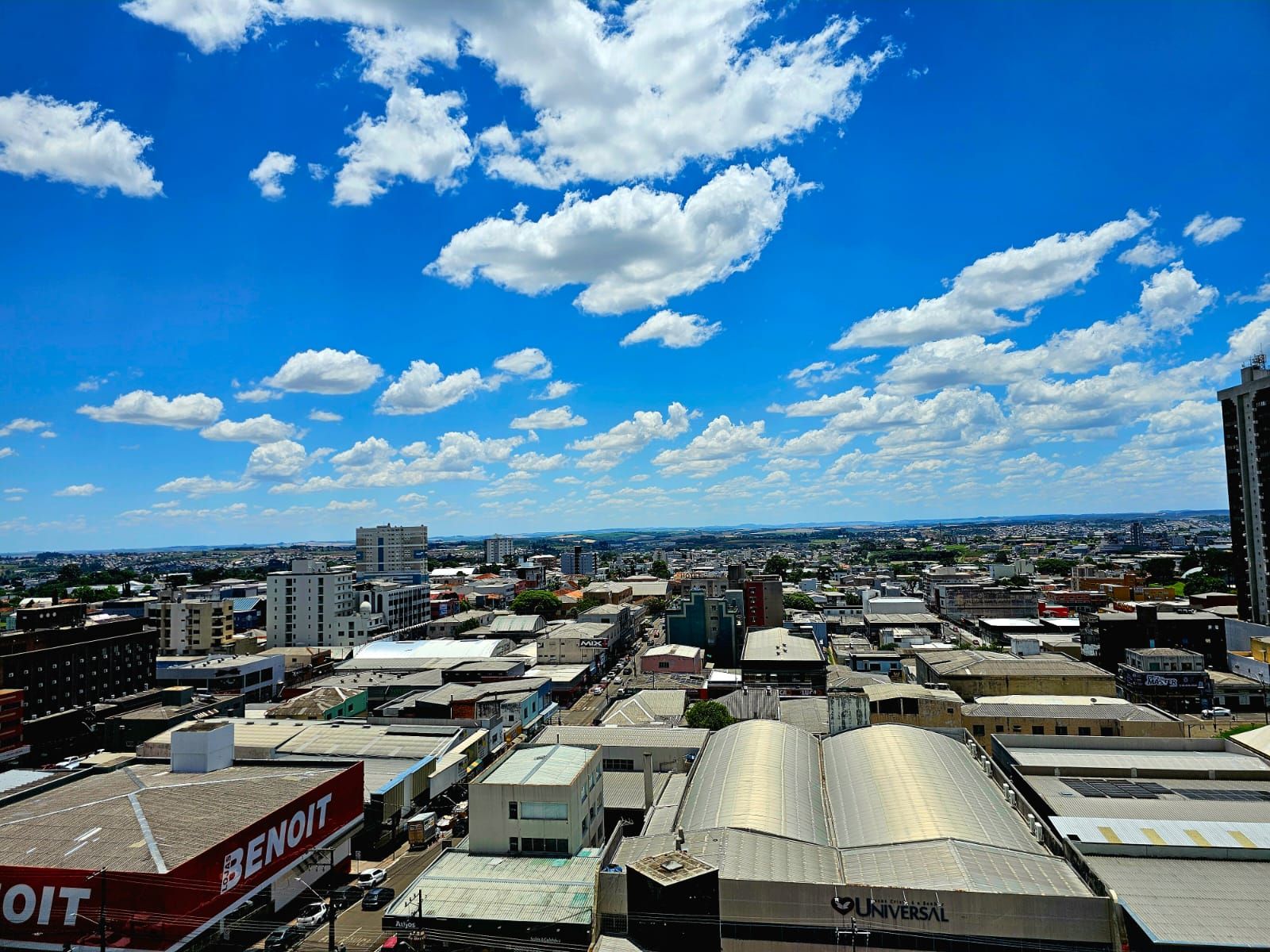 A cityscape with various buildings, including a large industrial facility with a curved roof and a prominent red and white sign.