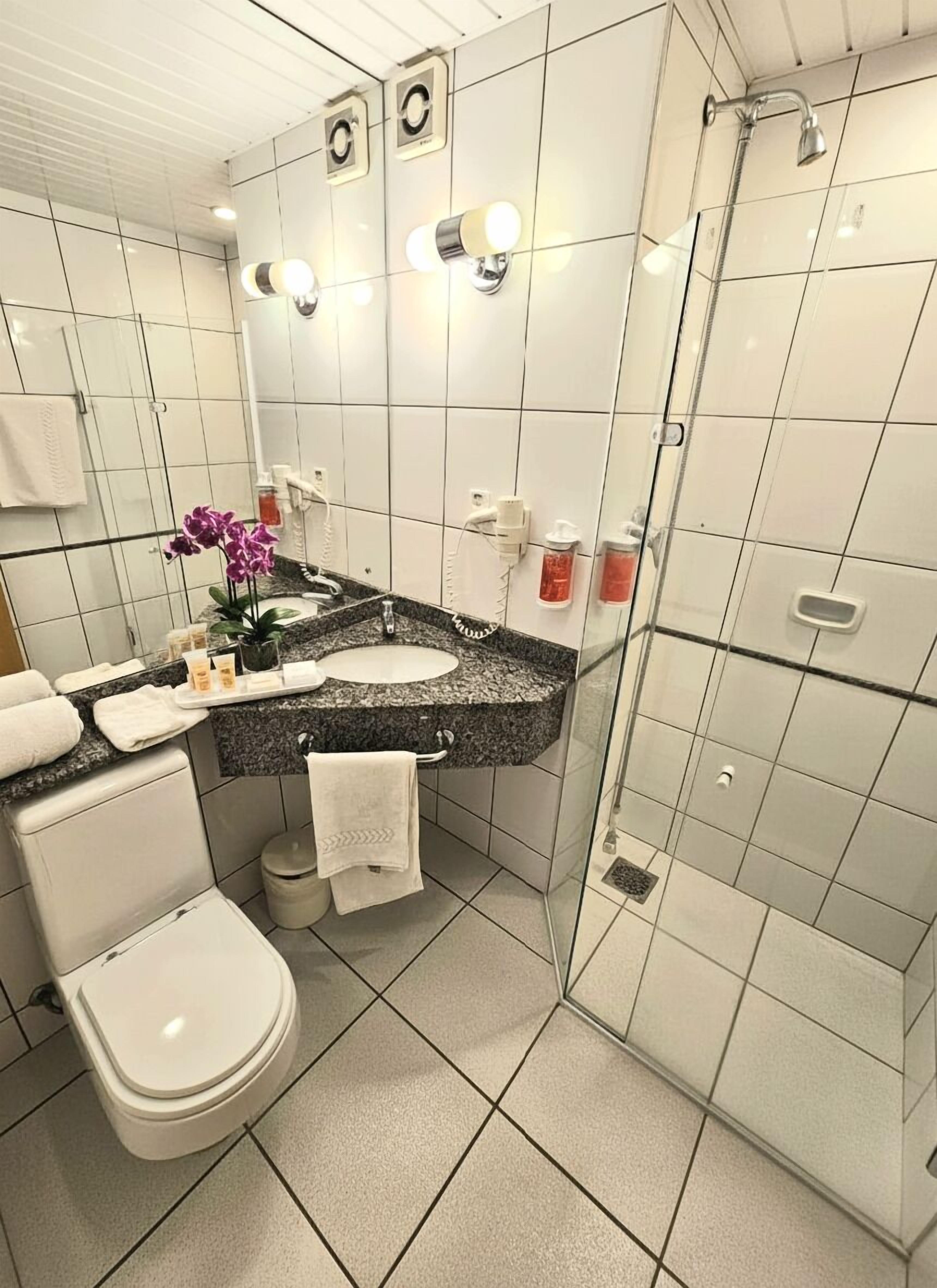 Un baño moderno con inodoro blanco, lavamanos con encimera de granito y cabina de ducha con mampara de vidrio.