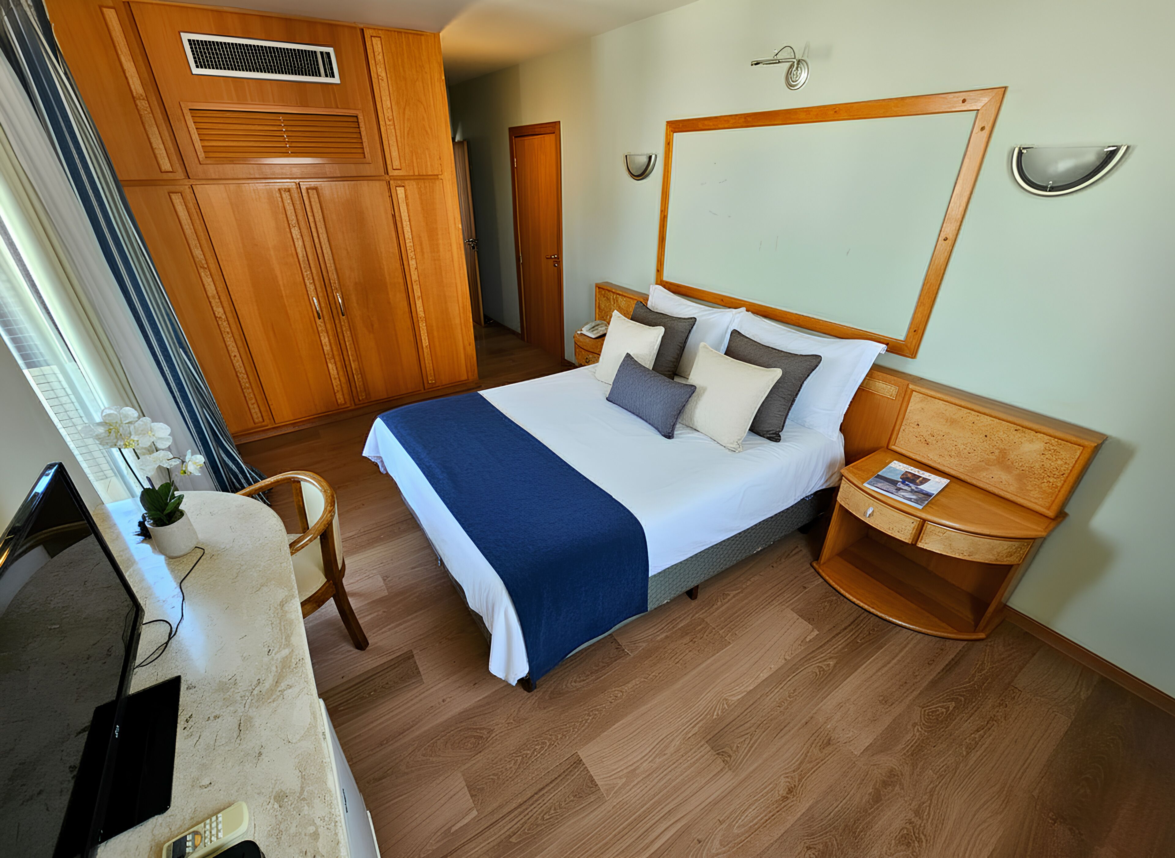Habitación de hotel con cama, armario de madera, mesita de noche y espejo en la pared.