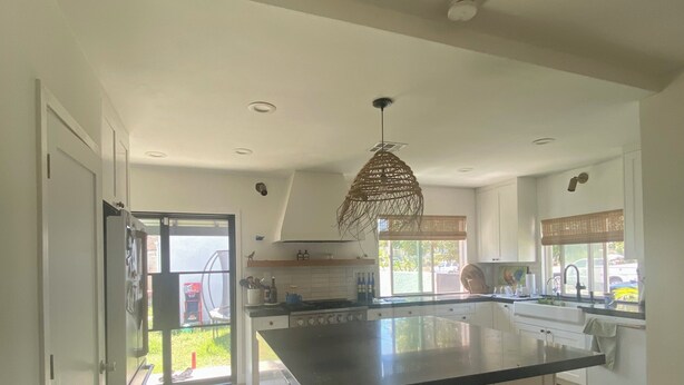 A spacious kitchen with a large island, wooden bar stools, and a hanging light fixture.