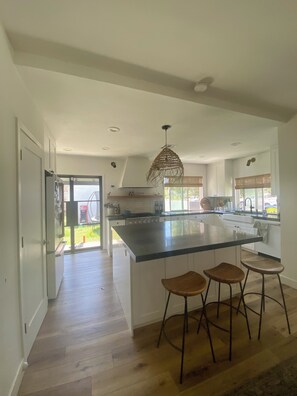 A spacious kitchen with a large island, wooden bar stools, and a hanging light fixture.