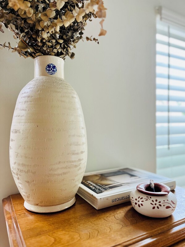 A white ceramic vase with a blue logo on a wooden surface next to a book and a small decorative item.