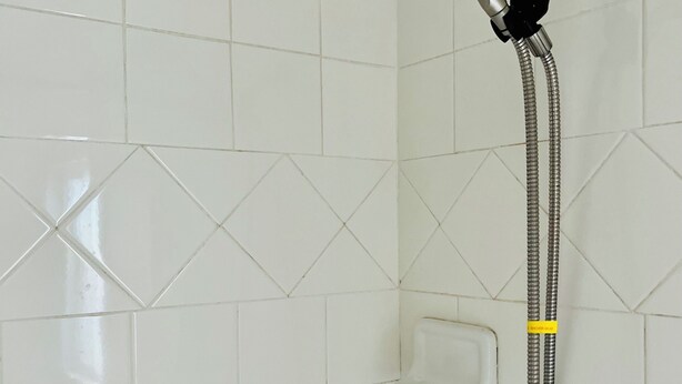 Ducha con cabezal de ducha manual y manguera flexible, instalada en una pared de azulejos.