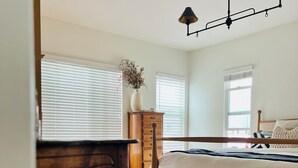 A bedroom with a bed, a wooden dresser, a small table, and a chandelier.