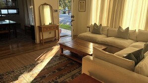 A living room with a sofa, coffee table, and a rug. There is a door leading outside, a window, and a small table with a mirror.