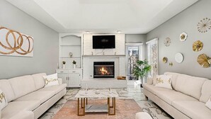 Una sala de estar moderna con chimenea, sofás blancos, una mesa de centro y decoración mural.