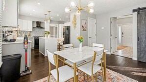 Una cocina moderna con armarios blancos, una isla central y un comedor con mesa de mármol y sillas doradas.