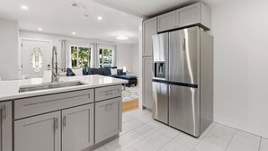 A modern kitchen with a stainless steel refrigerator, a large island with a sink, and light-colored cabinetry. - Happy Ours (New Smyrna Beach)