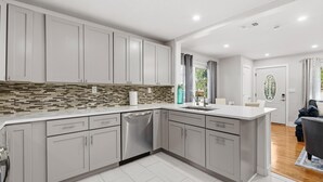 A modern kitchen with grey cabinets, a dishwasher, and a tiled backsplash. - Happy Ours (New Smyrna Beach)