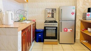 Eine kompakte Küche mit Einbauofen, Mikrowelle und Kühlschrank. Auf der Arbeitsplatte steht ein kleiner blauer Mülleimer und ein Wasserkocher.