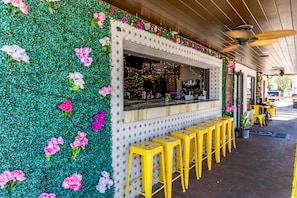 Ein Restaurant mit einer blumengeschmückten grünen Wand, einer Theke mit Sitzhocker und einem Deckenventilator.