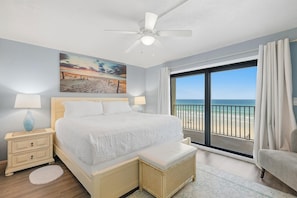 Ein Schlafzimmer mit Bett, Nachttisch, Lampe, einem Gemälde und Blick auf den Strand.