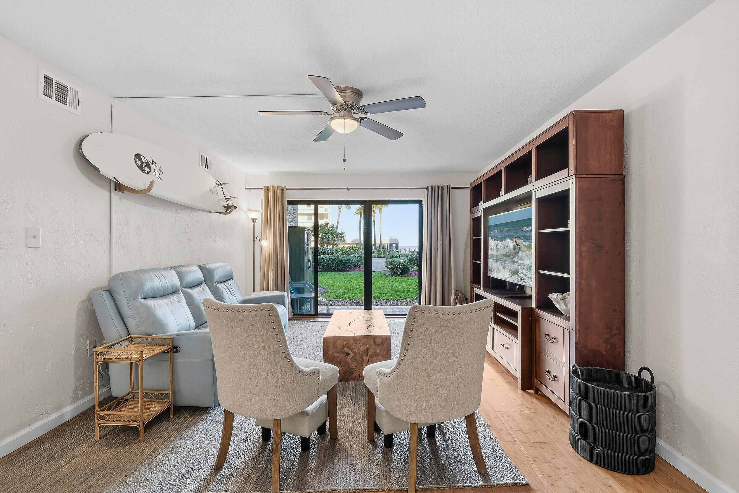 A modern living room with a sofa, two chairs, a coffee table, a ceiling fan, and a bookshelf.