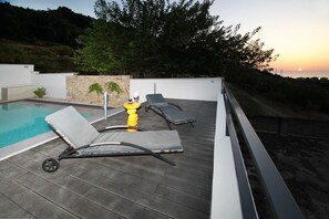 Ein Poolbereich auf dem Dach mit zwei Liegestühlen und einem gelben Schwimmkörper, umgeben von einer Steinmauer und Grünpflanzen.